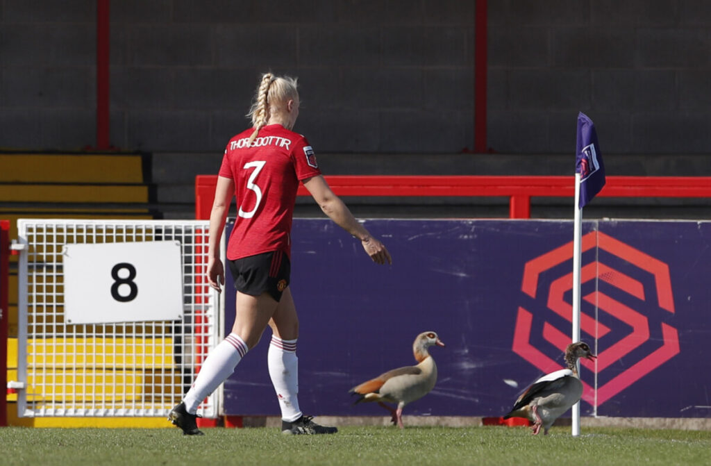 Manchester United's Maria Thorisdottir ushers ducks off the pitch during a match, right in front of the WSL logo