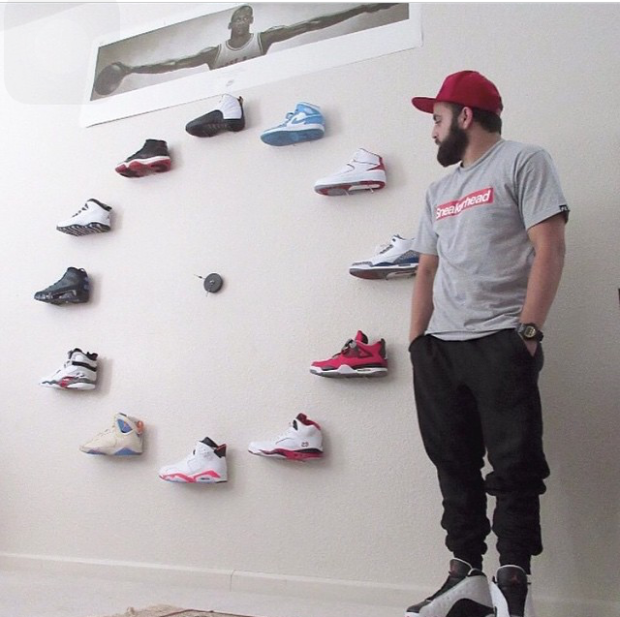A man wearing a red hat with his hands in his pockets looking at a wall display of shoes in the shape of a circle.