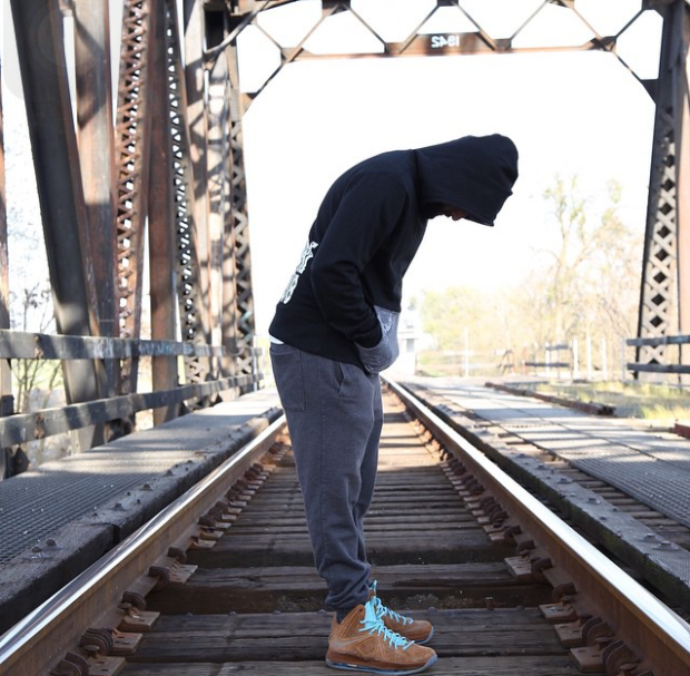 A man wearing a hooded sweat shirt standing on a train track with his hands in his pockets looking down.