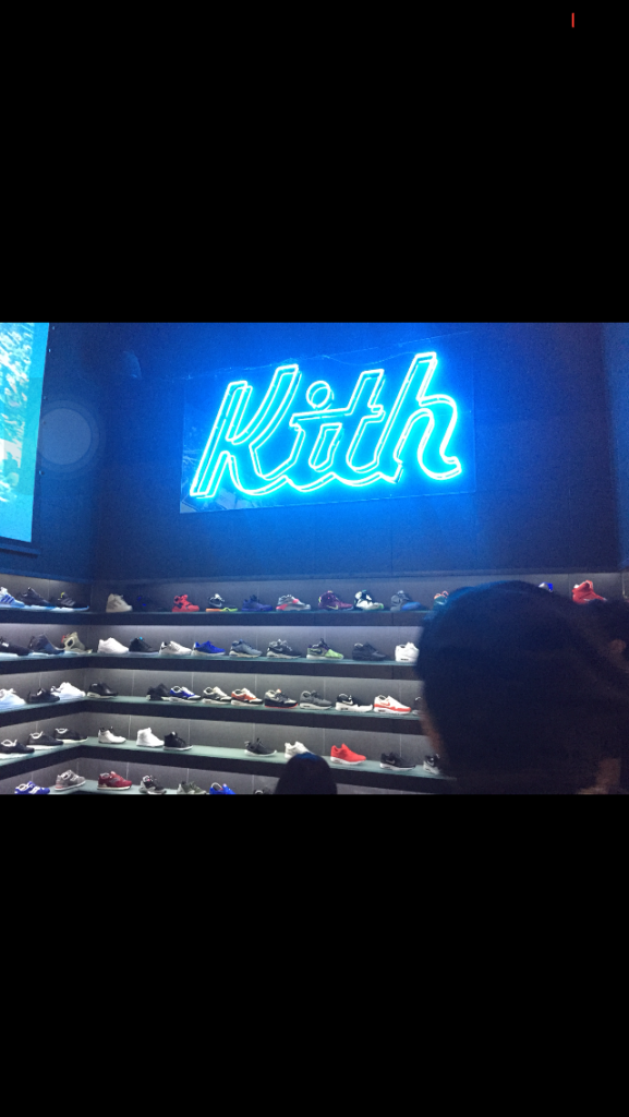 A neon blue light up sign that reads Kith inside a shoe store .