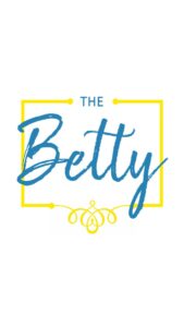 A white background with blue text reading "The Betty." "The," is spelt with straught block text and "Betty," is in cursive. There is a yellow box around the text as decor.