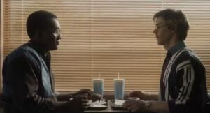 A black man and white man sitting across from each other at a restaurant.