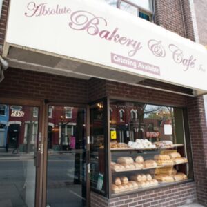 A photo of a bakery from the outside. There is a window with baked goods on display. There is a banner above the store which reads "Absolute Bakery and Cafe"
