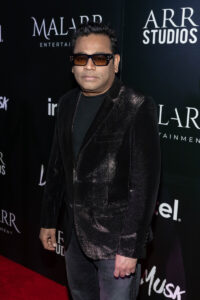 A man in a black velvet suit stands on the red carpet. He is wearing sunglasses and is in front of a poster which says Malarr studios and Le Musk.