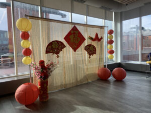Photo corner with cream-colored cloth and decorations attached to it. Flowers and lanterns which are yellow and red in colour surround it with some hanging on the rods on each side